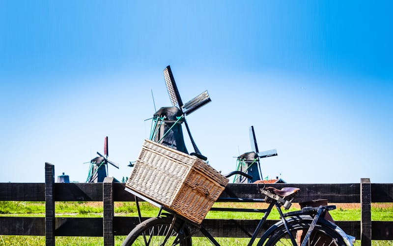HOlland-Rad lehnt an einem Zaun vor drei Windmühlen