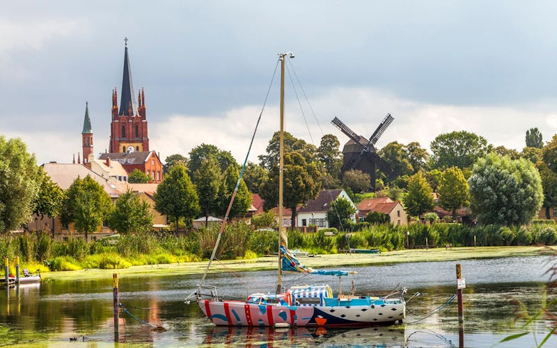 Boot auf Fluss, Windmühle und Kirche im Hintergrund