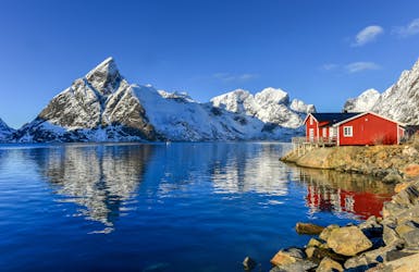 Schneebedeckte Berge mit rotem Holzhaus am Fjord